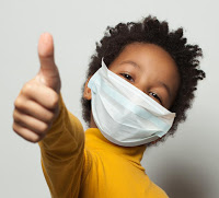 Happy African American black kid in medical protective face mask showing thumb up on white