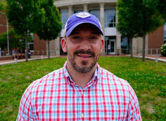 Smiling man with a goatee wearing a plaid shirt and a baseball cap